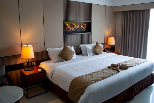 A cozy hotel room featuring a large bed with brown accents, side lamps, curtains, and a decorative wall piece above the headboard.