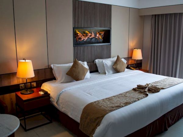 A cozy hotel room featuring a large bed with brown accents, side lamps, curtains, and a decorative wall piece above the headboard.