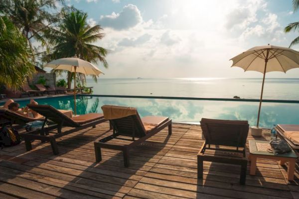 A serene poolside setting with lounge chairs, umbrellas, and a view of the ocean under a bright sky with scattered clouds.