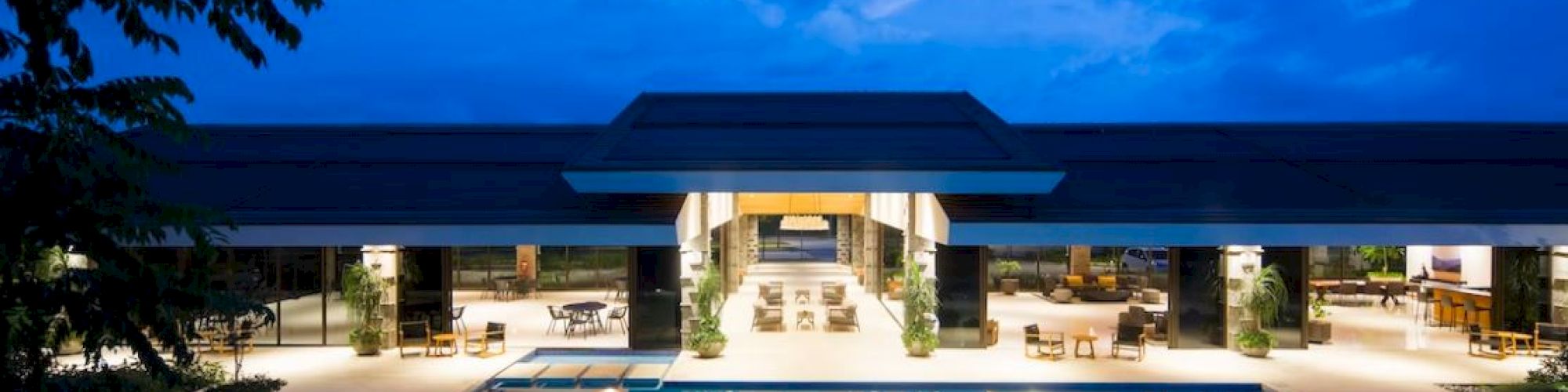 A luxurious building with a large illuminated pool and outdoor seating, set against a twilight sky.