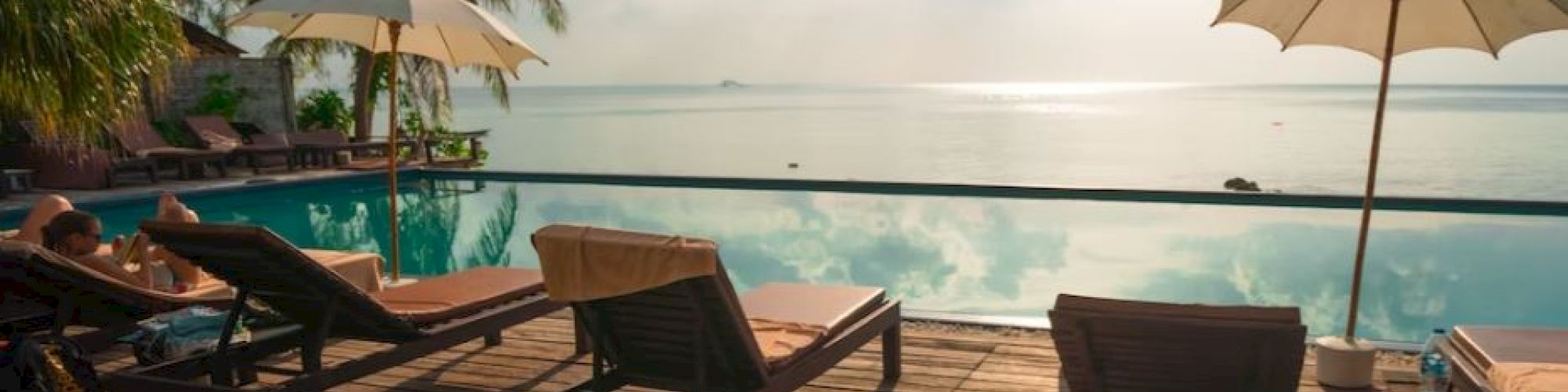 A serene poolside scene with deck chairs, umbrellas, and a view of the ocean under a partly cloudy sky.