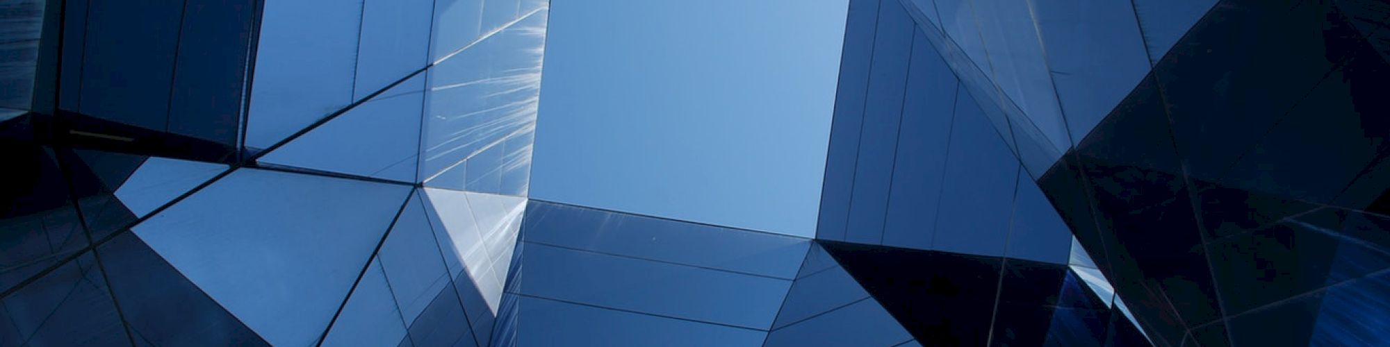 Abstract architecture featuring blue reflective glass panels forming a geometric pattern with a clear sky visible through the center.