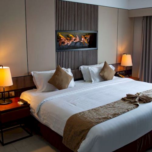 A luxurious hotel room with a large bed, decorative pillows, bedside lamps, and a modern wall feature above the headboard.