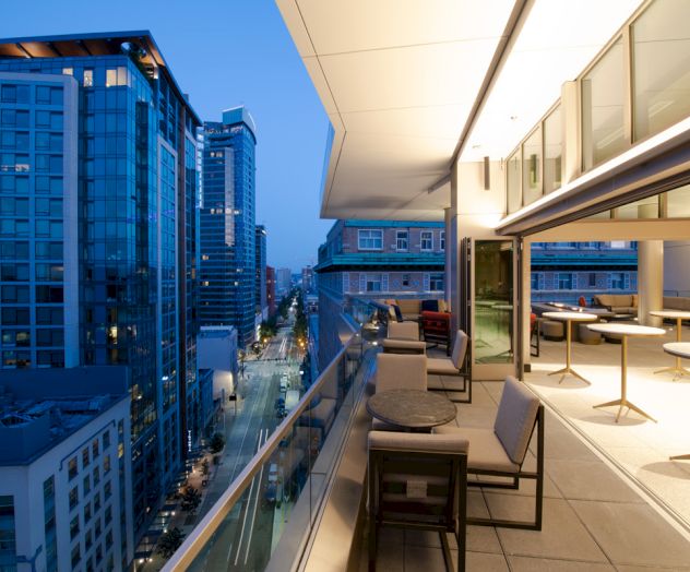 A modern balcony view of a cityscape at dusk, with tall buildings and a sleek, open-air dining area.