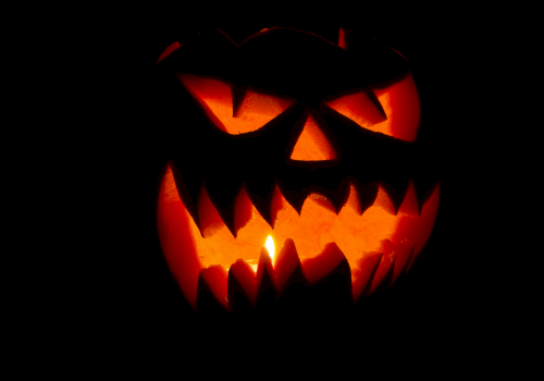 A glowing jack-o&rsquo;-lantern carved with a menacing grin, orange light flickering from within, casting eerie shadows in the darkness.