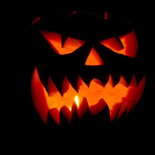 A glowing jack-o&rsquo;-lantern carved with a menacing grin, orange light flickering from within, casting eerie shadows in the darkness.