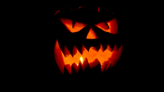 A glowing jack-o&rsquo;-lantern carved with a menacing grin, orange light flickering from within, casting eerie shadows in the darkness.