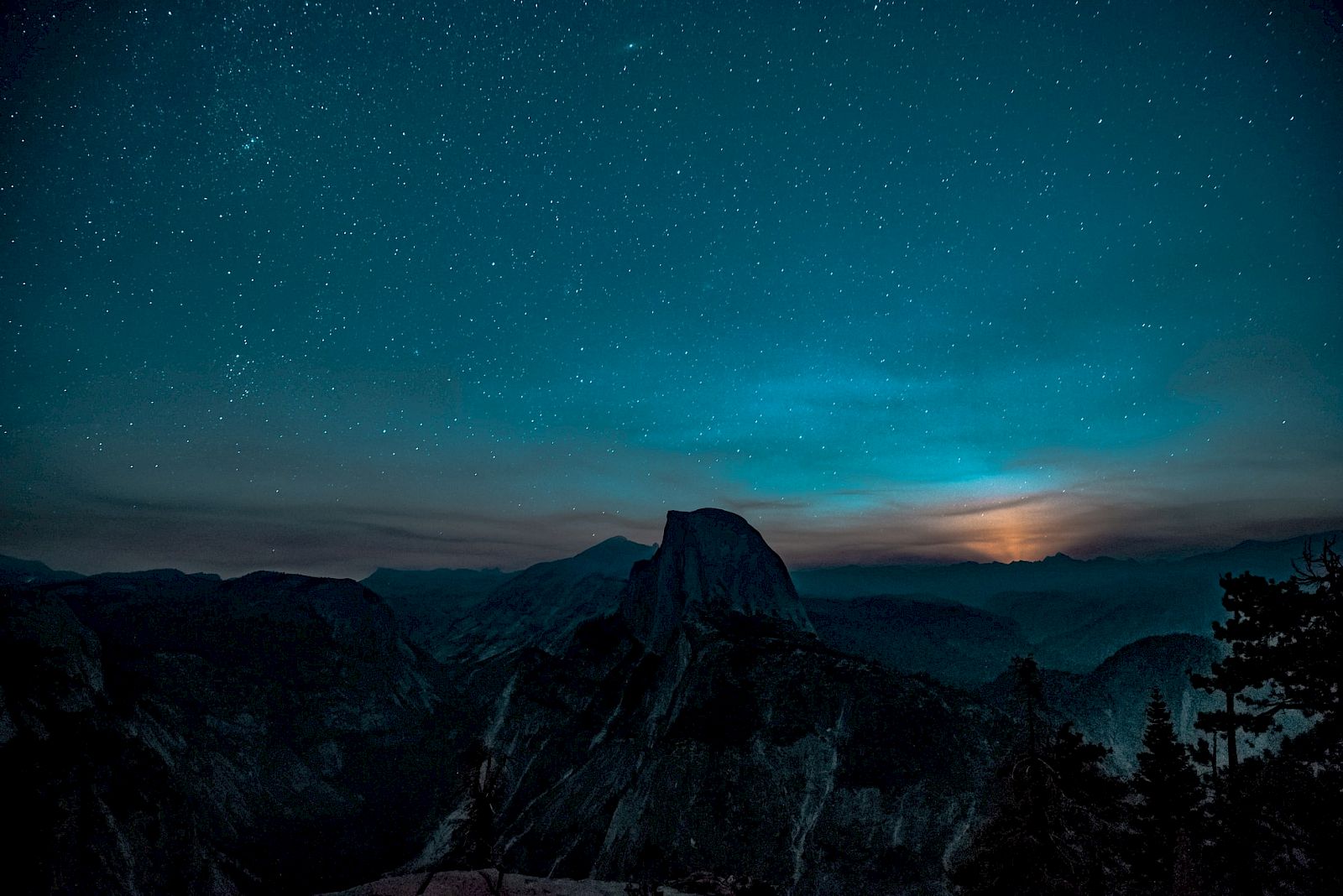 A starry night sky over a mountainous landscape with a glowing horizon, creating a serene and mystical atmosphere.