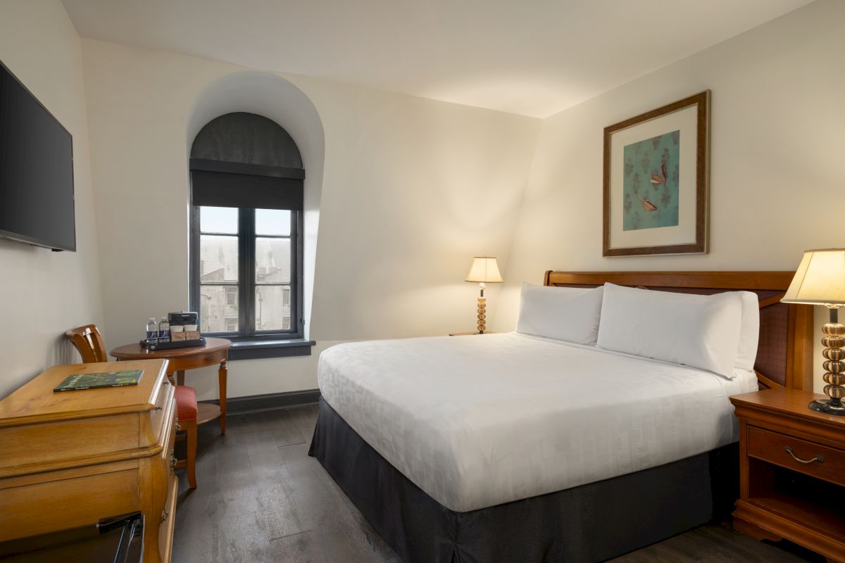 A hotel room with a bed, desk, TV, and window