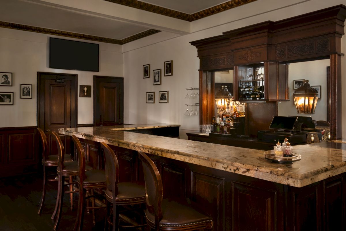 A dimly lit bar with a marble countertop, wooden barstools, and ornate mirror.