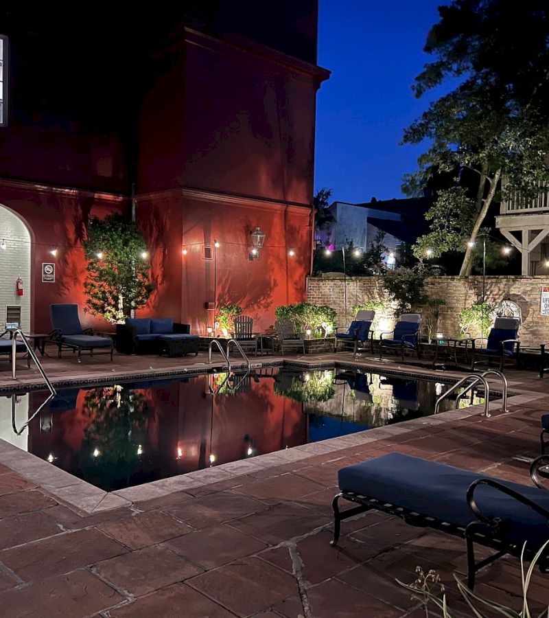A nighttime view of a hotel pool with lounge chairs and a red wall.