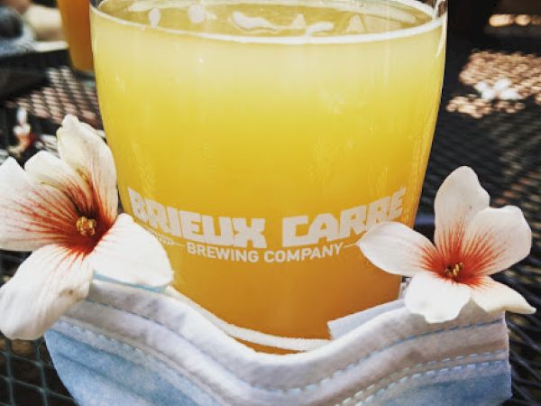 A glass of orange beer with a brewery logo, decorated with flowers and placed on a face mask.