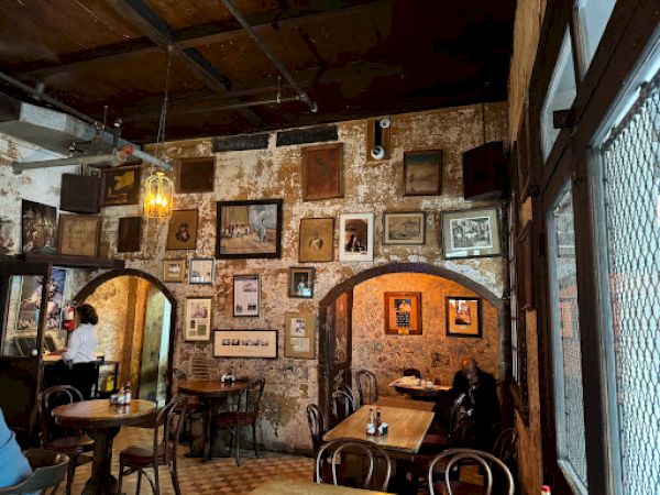 A cozy cafe with rustic decor, framed pictures on the wall, wooden tables, chairs, and a person at a table in a warm ambiance.