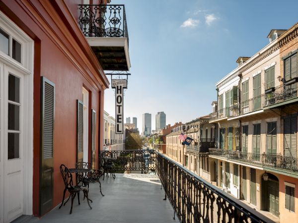 A balcony view of a historic street with a "HOTEL" sign, showcasing colorful buildings and a city skyline in the background.