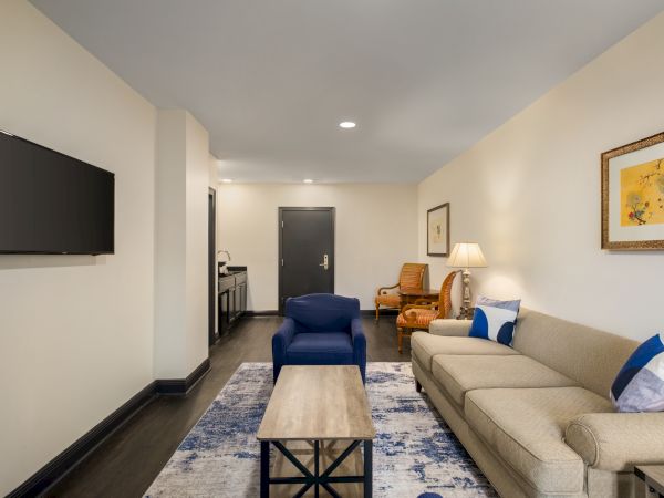 A modern living room with a beige couch, blue chairs, wall art, a television, and a coffee table, decorated with a blue-patterned rug.