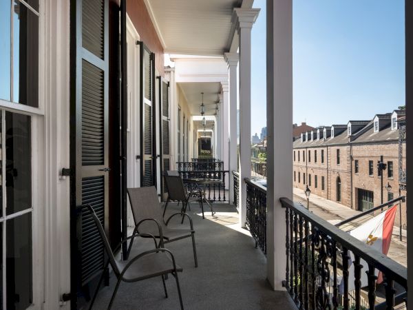 A long balcony with chairs, iron railings, and a view of a street with brick buildings on a clear day.