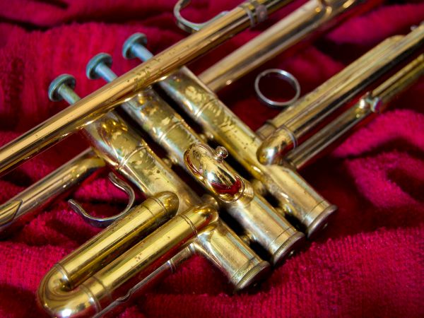 The image shows a brass trumpet resting on a red fabric background.