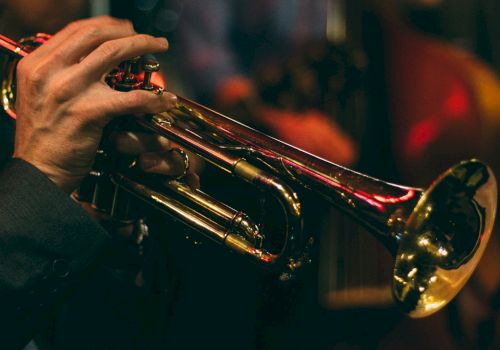 The image shows a person playing a trumpet, with a blurred background suggesting a musical performance or practice setting.