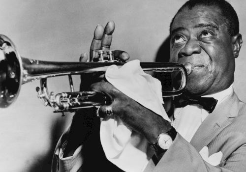 A black-and-white photo of a jazz trumpeter in a suit, playing his horn with a white napkin, smiling while bowing the notes.