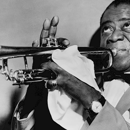 A black-and-white photo of a jazz trumpeter in a suit, playing his horn with a white napkin, smiling while bowing the notes.