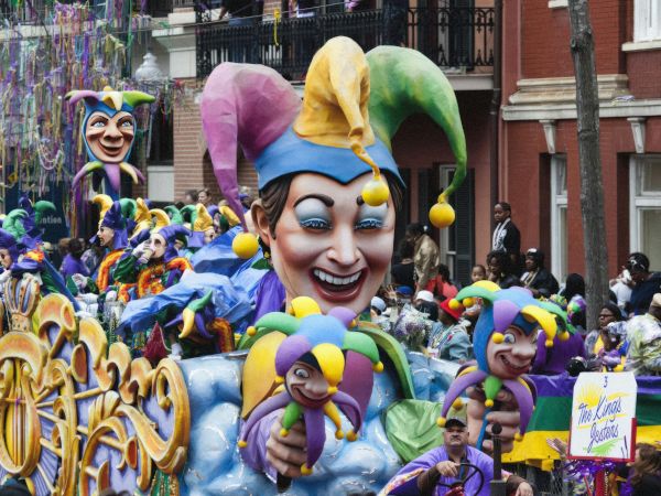 A lively parade with colorful floats, jester figures, and people dressed in costumes, creating a festive atmosphere.
