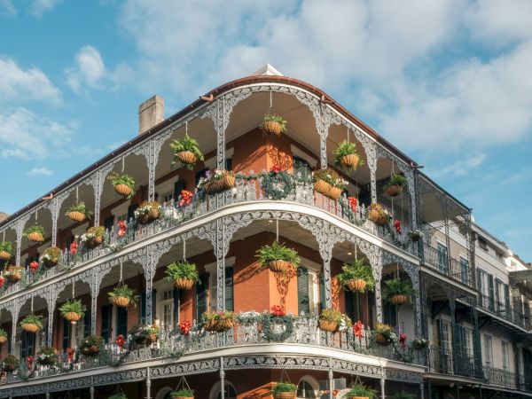 A historic building with ornate ironwork balconies and hanging plants under a blue sky with scattered clouds.