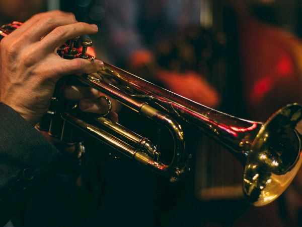 A person is playing a brass trumpet, captured in a dimly lit setting, likely at a live music performance or jazz club.