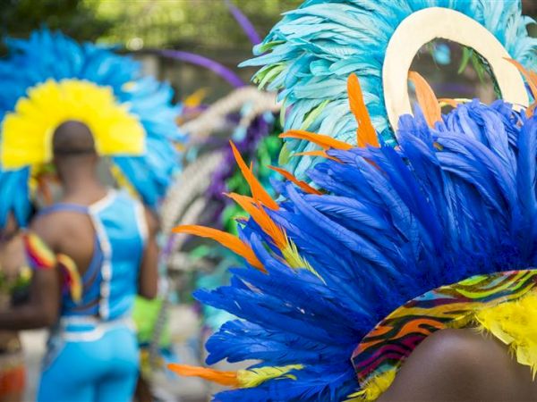 People are wearing vibrant costumes with colorful feathered headdresses, possibly at a parade or festival.