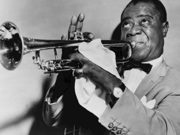 A man in a suit plays the trumpet passionately. He holds a cloth in his hand, and his expression shows concentration and joy.