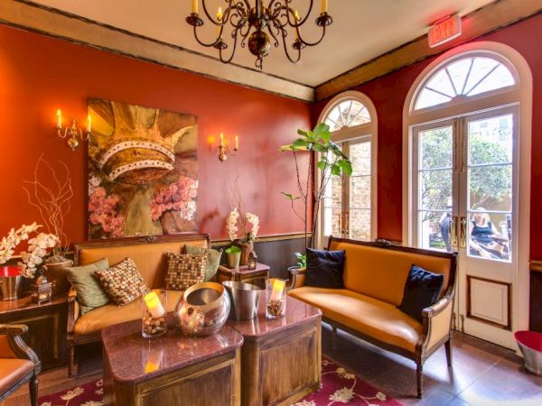 A cozy, elegant lounge with red walls, leather seating, chandeliers, and a doorway to an outside area; plants and candles add warm ambiance.