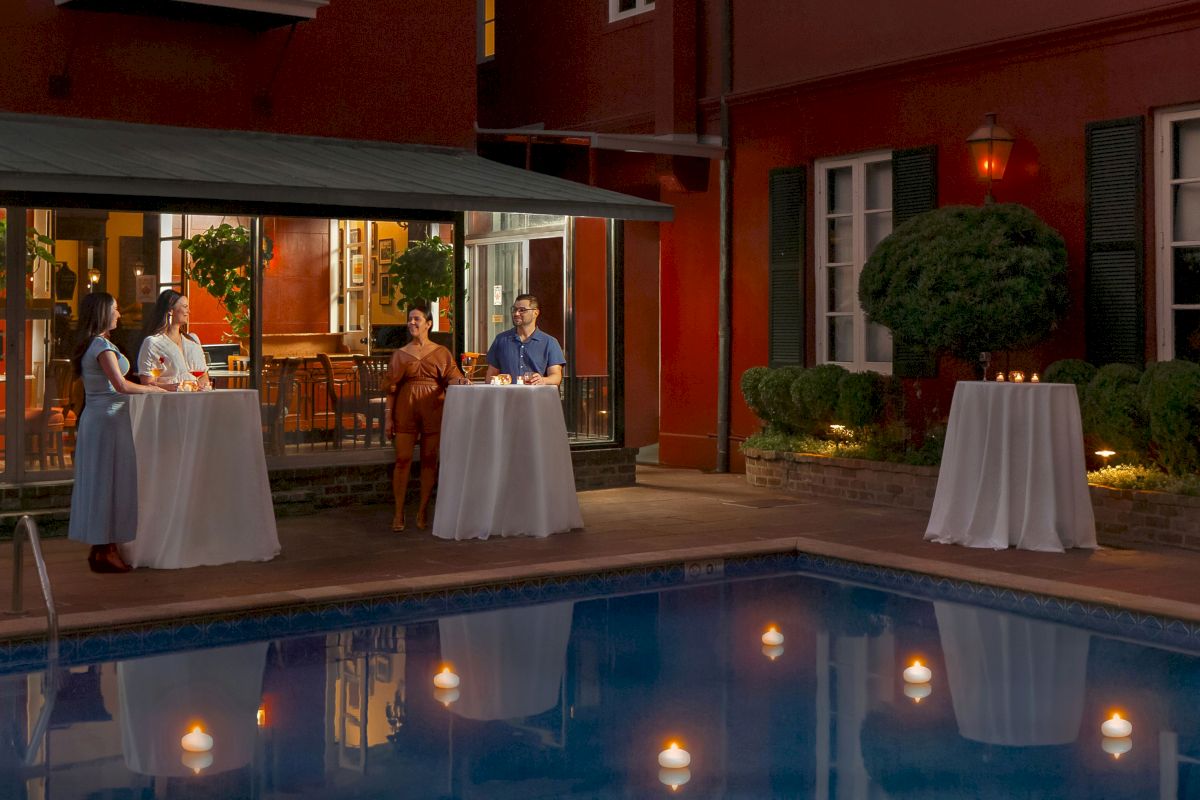 A nighttime scene of a poolside bar with white tables and candlelight