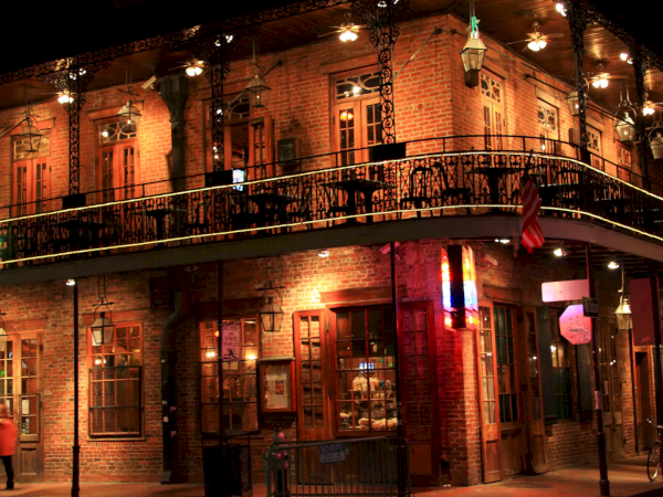 Old brick building with a lit balcony and hanging lanterns at night, looks like a cozy street corner bar or cafe. end.