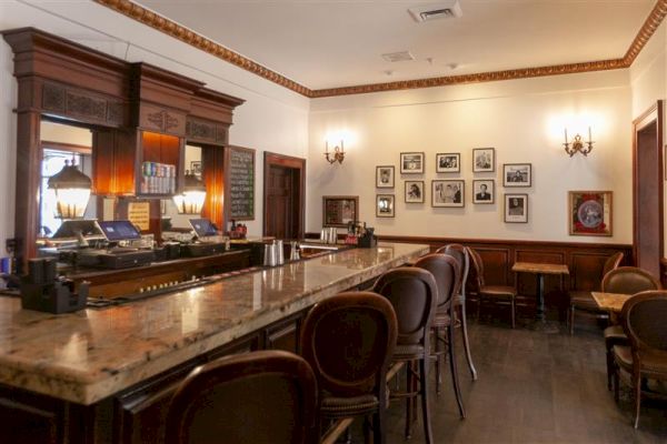 A wide view of a bar with a marble countertop, bar stools, and framed pictures on the walls.