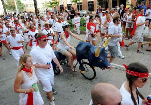 A large crowd in red-and-white marches in a city street, celebrating beside a blue-and-black dragon ride in a parade.