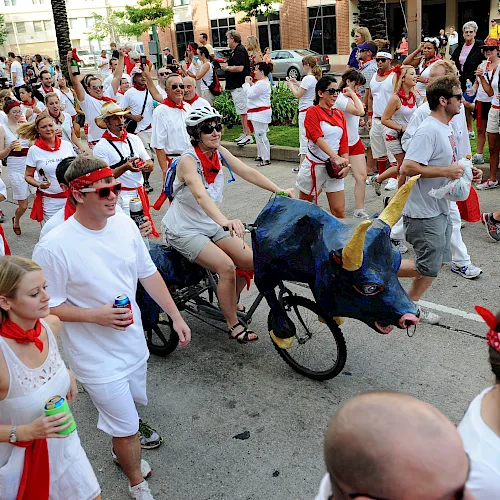 A large crowd in red-and-white marches in a city street, celebrating beside a blue-and-black dragon ride in a parade.