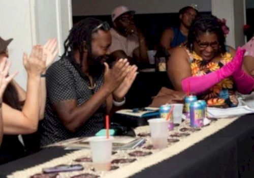 A group of people clap and smile at a banquet table while eating, in a lively celebration.