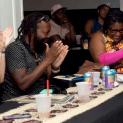 A group of people clap and smile at a banquet table while eating, in a lively celebration.