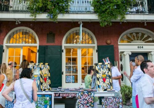 A crowd browses colorful tote bags and souvenirs at a street booth outside a brick building numbered 604.