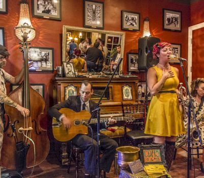 A live music performance with a woman singing and a man playing guitar in a room with red walls.
