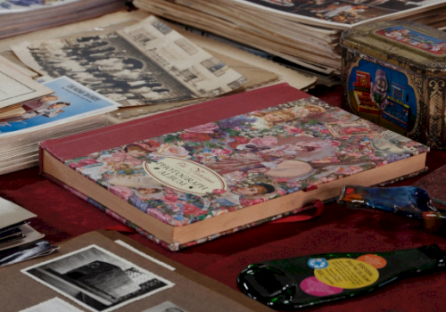 A table display of old books and photo prints, with a floral hardback, vinyl records, and a decorative tin box.