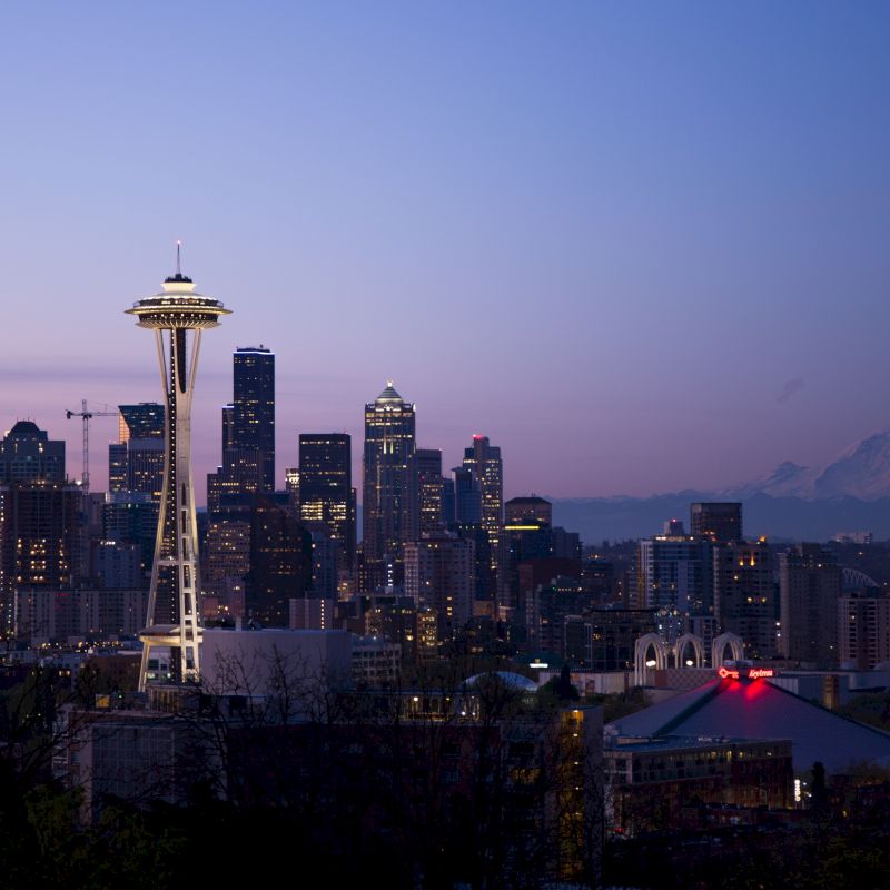 Seattle skyline at dusk with the Space Needle prominent, set against Mount Rainier in the background.