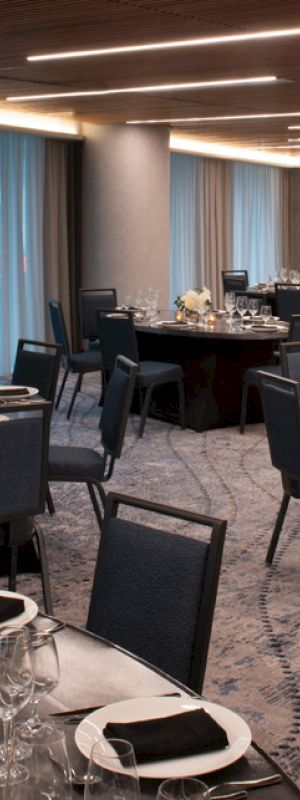 The image shows a banquet hall with round tables, black chairs, place settings, and dim lighting, giving an elegant atmosphere.