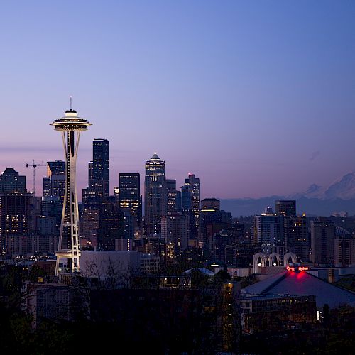 Seattle skyline at dusk featuring the Space Needle, with Mount Rainier visible in the background against a colorful sky.