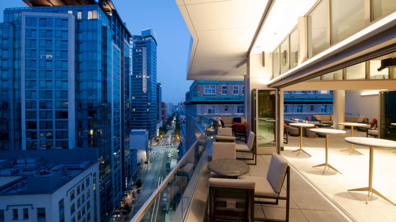 A modern rooftop terrace with seating overlooks a cityscape with tall buildings, captured during twilight.