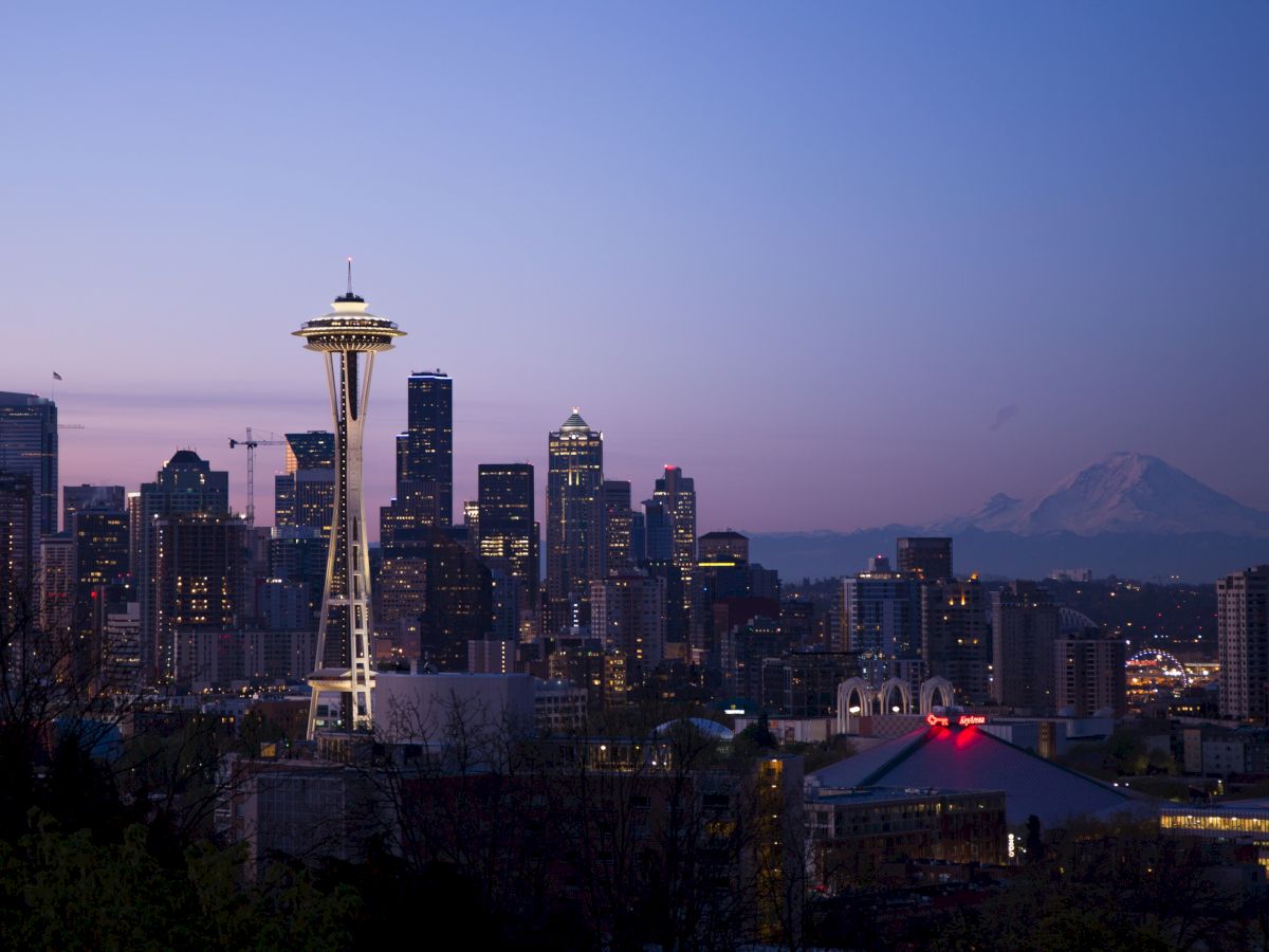 The image shows a city skyline at dusk with the Space Needle prominently visible and a mountain in the background.